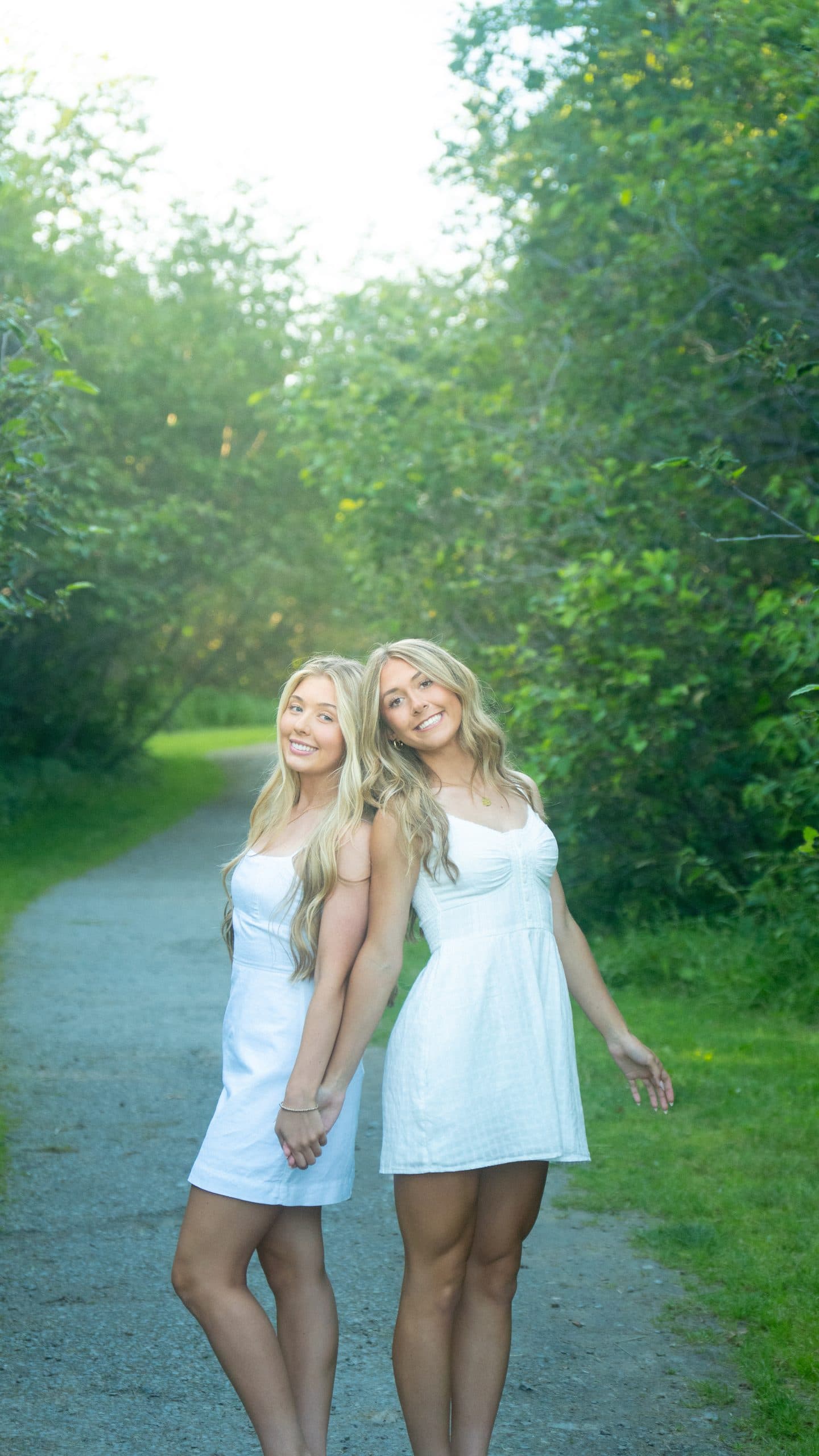 Two friends standing back to back on a wooded path in summer