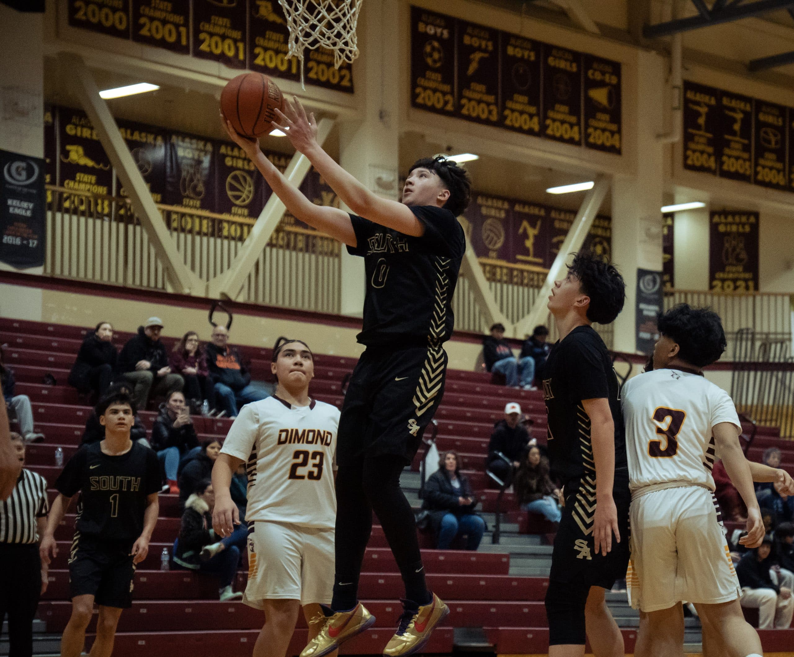 Basketball player rising for a layup at the rim beneath rows of maroon state championship banners